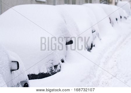 horizontal side view of a row of cars covered completely in a city parking lot winter time