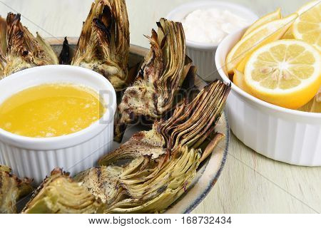 Closeup  of a palte full of grilled artichokes with butter, lemons, and mayonnaise.