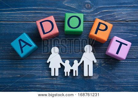 Cubes with word ADOPT and figure in shape of family on color wooden background