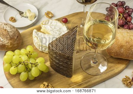 A photo of a glass of white wine with cheese, white and rye bread, red and white grapes, and walnuts, at a wine pairing. Selective focus