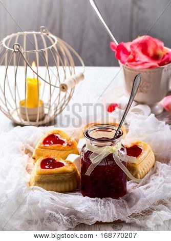 Cupcakes from curd in the form of hearts. Jar with raspberry jam. Cup with rose petals. Candle in the cage