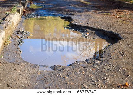 The bad asphalted road with a big pothole filled with water.