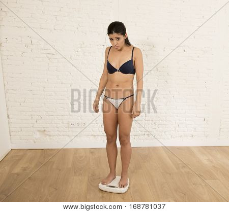 young fit skinny woman or teen girl checking body weight on scale finding herself fat looking desperate obsessed with overweight and weight loss in anorexia and bulimia nutrition disorder