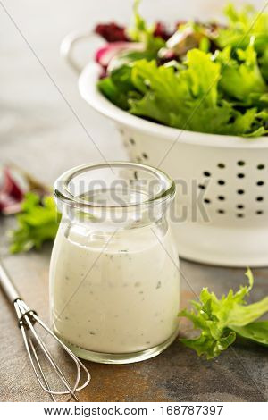 Homemade ranch dressing in a small jar with fresh greens