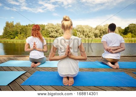 fitness, sport, yoga and healthy lifestyle concept - group of people exercising in reverse prayer pose on river or lake berth