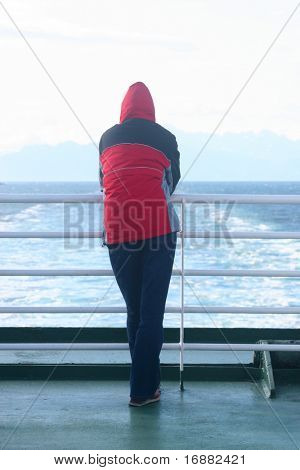 uomo solo nella cappa in piedi presso la nave e guardando il mare