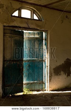 Old blue door is ajar and through the slit pouring sunlight.