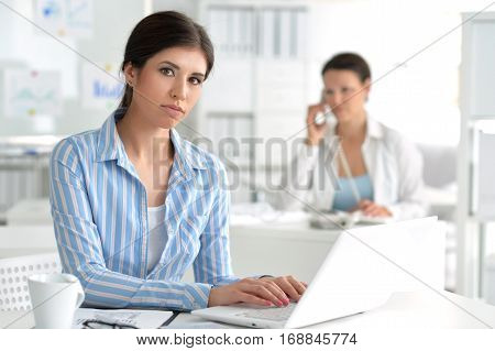 Portrait of a young female office worker, using laptop