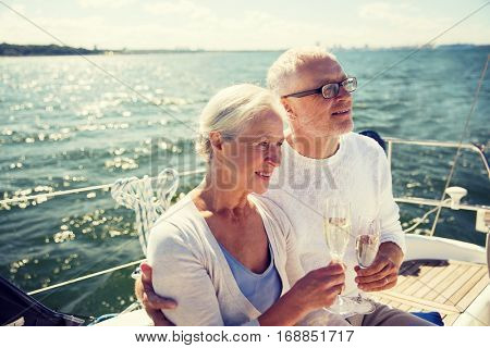 sailing, age, tourism, travel and people concept - happy senior couple drinking champagne on sail boat or yacht deck floating in sea