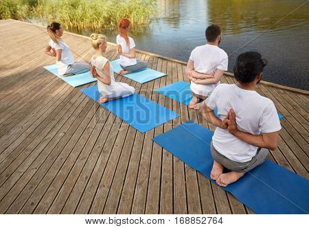 fitness, sport, yoga and healthy lifestyle concept - group of people exercising in reverse prayer pose on river or lake berth