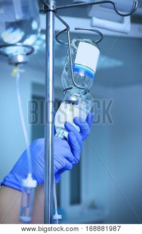 Doctor's hands and infusion drip in hospital on blurred background