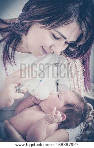 Smiling Mother Feeding Milk To Baby From Bottle At Home