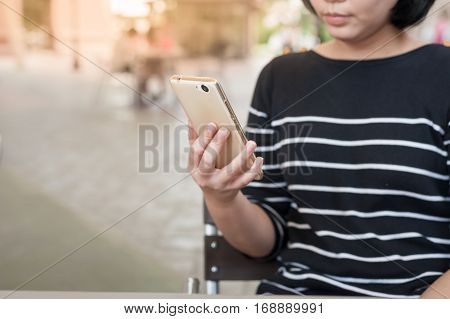 Weekend activity scene of adult Asian woman watiching on mobile phone at coffee shop. Urban lifestyle with technology concept.