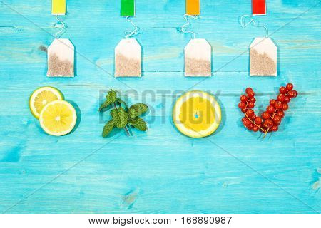 Flavored teabags fresh fruit top view on aquamarine wood table with copy space - Mint leaf lemon orange and cranberries colorful still life composition light blue background image from above