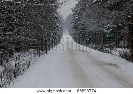 The photo shows a forest road. It's winter. Earth and tree branches cover layer of snow. The surface of the road is unpaved, uneven and bumpy. Wiedoczne are clear rut.
