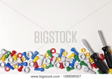 Construction tools frame on white background. Colorful toys plastic bolts, nuts and screwdrivers arranged in line. Top view. Flat lay. Copy space text