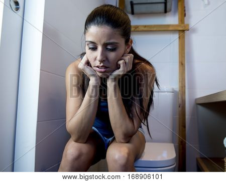 young sad and depressed bulimic woman feeling sick sitting in toilet WC looking desperate and ill in pregnancy and depression concept
