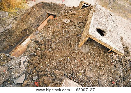 Rusty water pipe in trench and concrete construction on heap of earth.