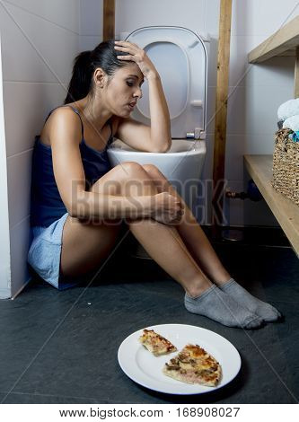 young sad and depressed bulimic woman feeling sick guilty after vomiting and throwing up kneeling on floor of toilet WC guilty eating pizza in nutrition disorder bulimia and anorexia concept