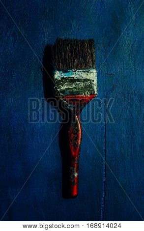 An used, big paint brush with stains on blue background. A still life object.