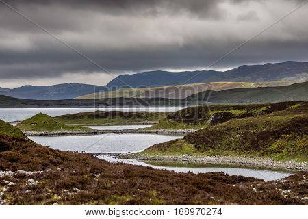 North Coast, Scotland - June 6, 2012: Irregularly shaped gray-water Loch Eriboll under dark cloudy skies. Wide shot showing land tongues background mountains and green and brown vegetation.
