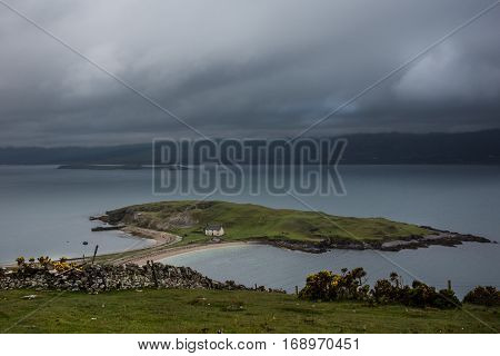 North Coast Scotland - June 6 2012: Small green island in Loch Eriboll connected with a short dam and featuring a white fisherman house. Cloudy foggy sky bluish water mountainous background.