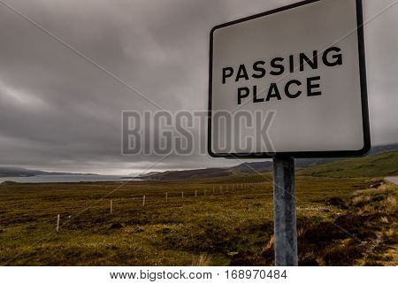 North Coast Scotland - June 6 2012: Typical road sign black on white announcing a passing place on the narrow roads under rainy cloudy gray sky. Set along Loch Eriboll seen in back. Green and brown pasture.