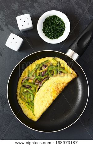 Omelette with green bell pepper and red onion in frying pan photographed overhead on slate with natural light