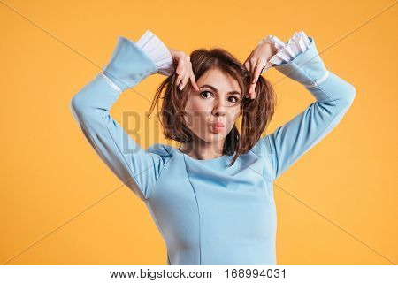 Playful comical young woman joking and making funny face over yellow background