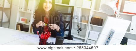 A Beautiful Young Girl Sits In The Office At The Table And Holds A Yellow Marker In Her Hands.