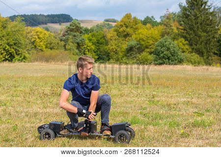 Caucasian Teenage Boy Rides Electrical Mountainboard In Grass Field