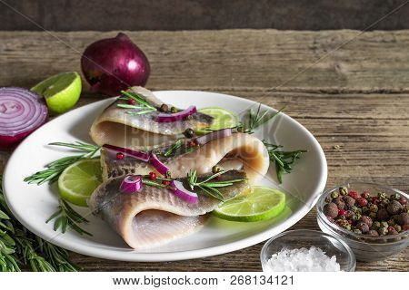 Marinated Herring Fillet With Pepper, Rosemary, Onion And Lime In A Plate On Rustic Wooden Backgroun