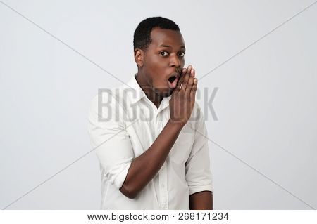 Young African Man Whispering A Secret Behind Heis Hand.