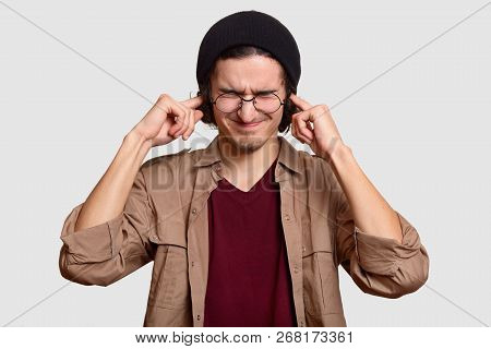 Stressful Teenager Wears Black Har And Beige Shirt, Pluggs Ears, Ignores Loud Sound Coming From Nois