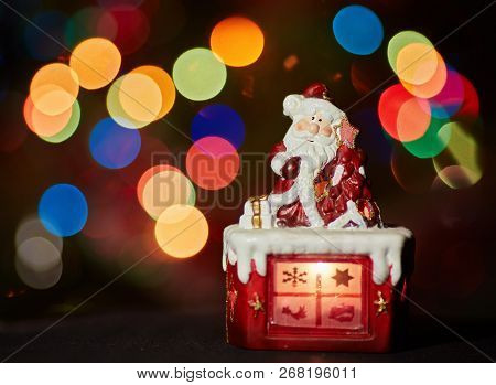 Santa Claus Statuette Doing An Exercise Waiting For Christmas. Colored Bokeh