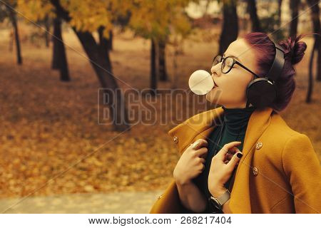 Cute Young Girl Listening To Music On Headphones In Autumn Park. The Girl Has Eggplant Hair. She Is 