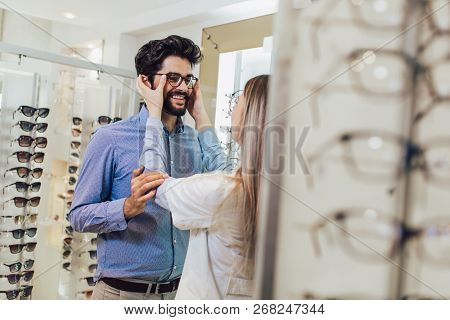 Femaale Ophthalmologist Helping Man To Choose Glasses In Optical Store