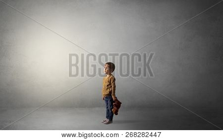 Little waggish kid staying alone in a big empty room with his plush