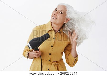 Charming Elegant Grandmother With Grey Hair Standing In Trendy Yellow Coat Bending Right, Making Las