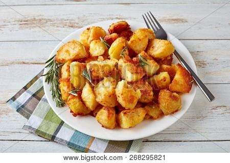 Close-up Of Crispy Roast Potatoes With Spices And Rosemary Served On A White Dish With Napkin And Si