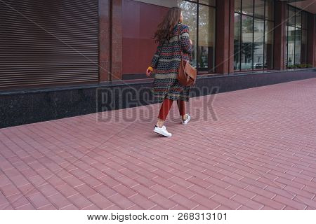 Portrait Of A Stylish Young Woman Walking In European City. New Street Red Pavement And Murble. Side