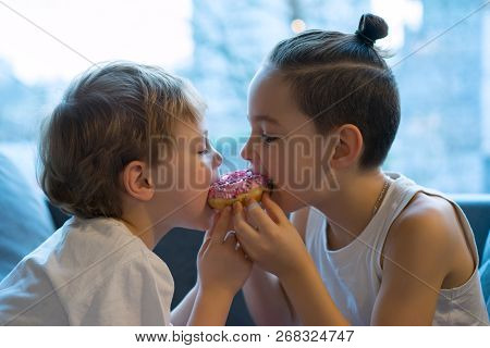 Two Kids Bite Off A Donut And Having Fun. Two Boys Together Bite From The Donut. Children Enjoy A Do