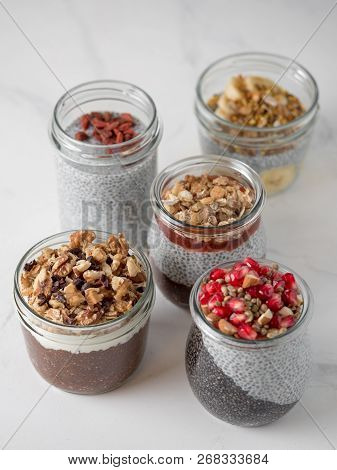 Set Of Chia Pudding In Different Glass Jars On White Marble. Assortment Of Chia Puding With Differen