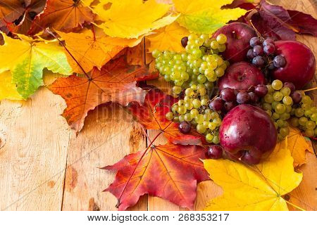 Red Juicy Ripe Apples With Grapes And Autumn Maple Leaves On A Wooden Background