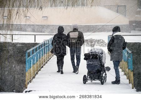Passers-by On The Bridge During A Snowstorm Against The Background Of Urban Buildings. Selective Foc