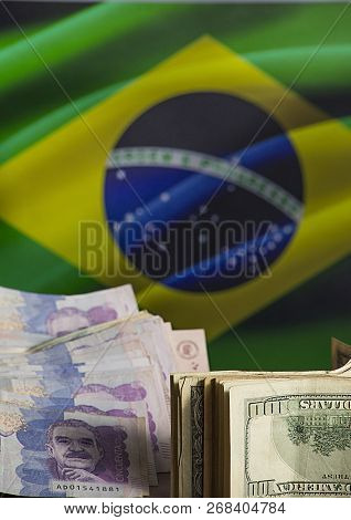 Planning Trip To Brazil- Dollars And Colombian Money With Flag Of Brazil In The Background
