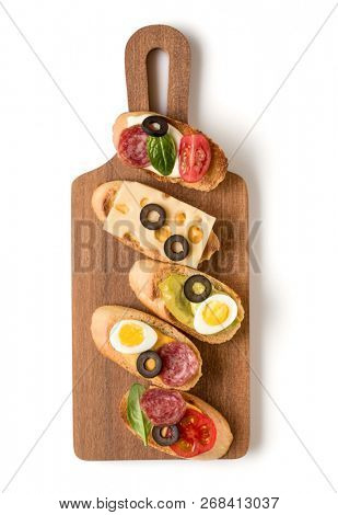 Open faced sandwich canape or crostini on a wooden serving board isolated on white background closeup. Top view.