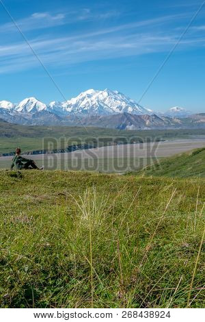 Young Adult Woman Sits On A Hill Looking Out At Mount Denali (mckinley) In Denali National Park. Con