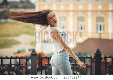 Portrait Of A Girl In Jeans And A T-shirt On The Background Of The Building In The Evening On A Summ