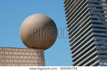 BARCELONA, SPAIN - APRIL 17, 2018: The Esfera (sphere) sculpture by architect Frank Gehry at Port Olimpic with the Mapfre Tower in the background. The artwork was created in 1992 for the Olympic Games